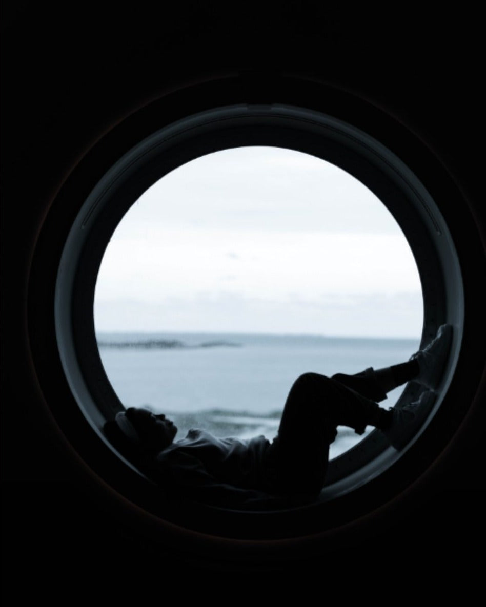 Geri, silhouetted in a ship's porthole above the sea