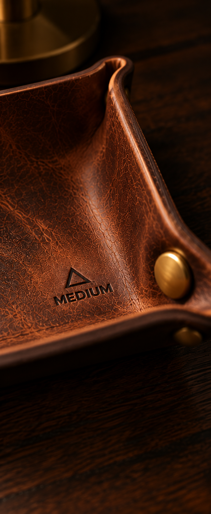 Close-up detail of the debossed MEDIUM mark and solid-brass stud on the Heritage Brown valet tray